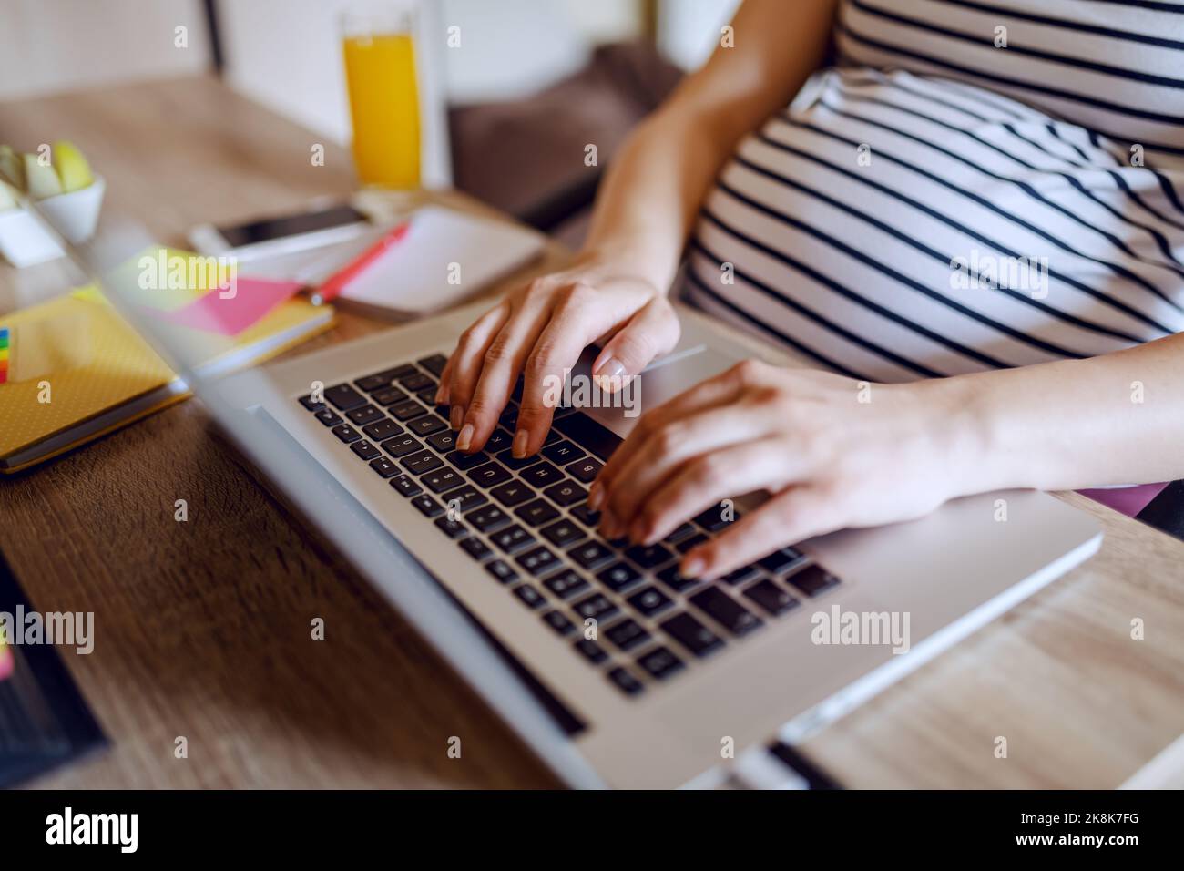 Jeune femme enceinte caucasienne assise à une table au bureau à domicile et dactylographiant sur un ordinateur portable. Femmes enceintes actives concept. Banque D'Images