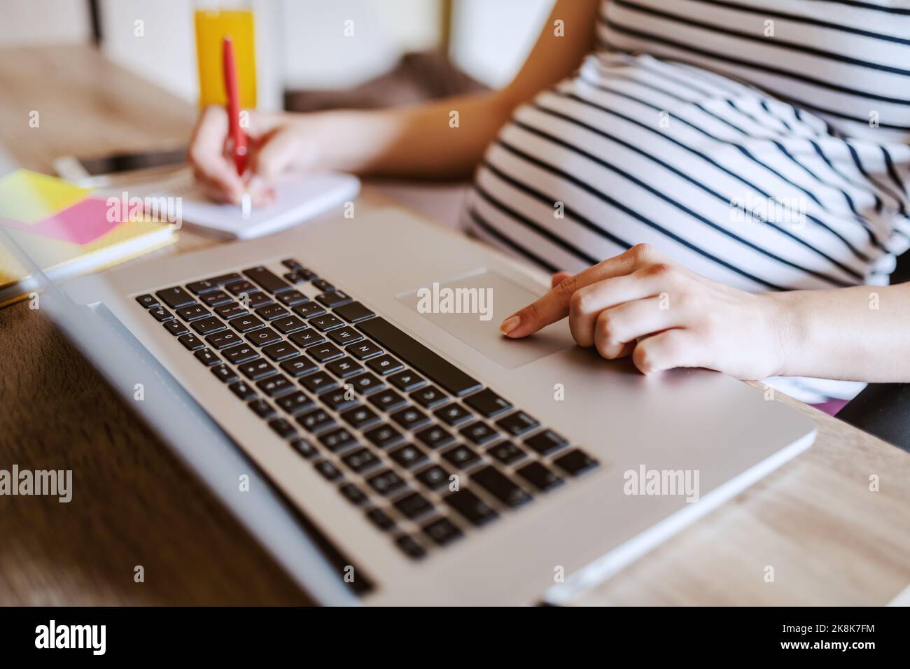 Femme enceinte assise à une table et écrivant dans un carnet. Sur le jus de bureau et l'ordinateur portable. Concept de femme enceinte de travail. Banque D'Images