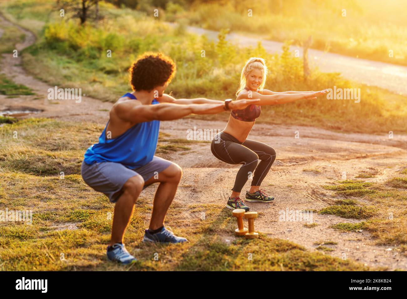 Couple sportif souriant dans des vêtements de sport faisant l'endurance en position de squat dans la nature le jour ensoleillé d'été. Banque D'Images