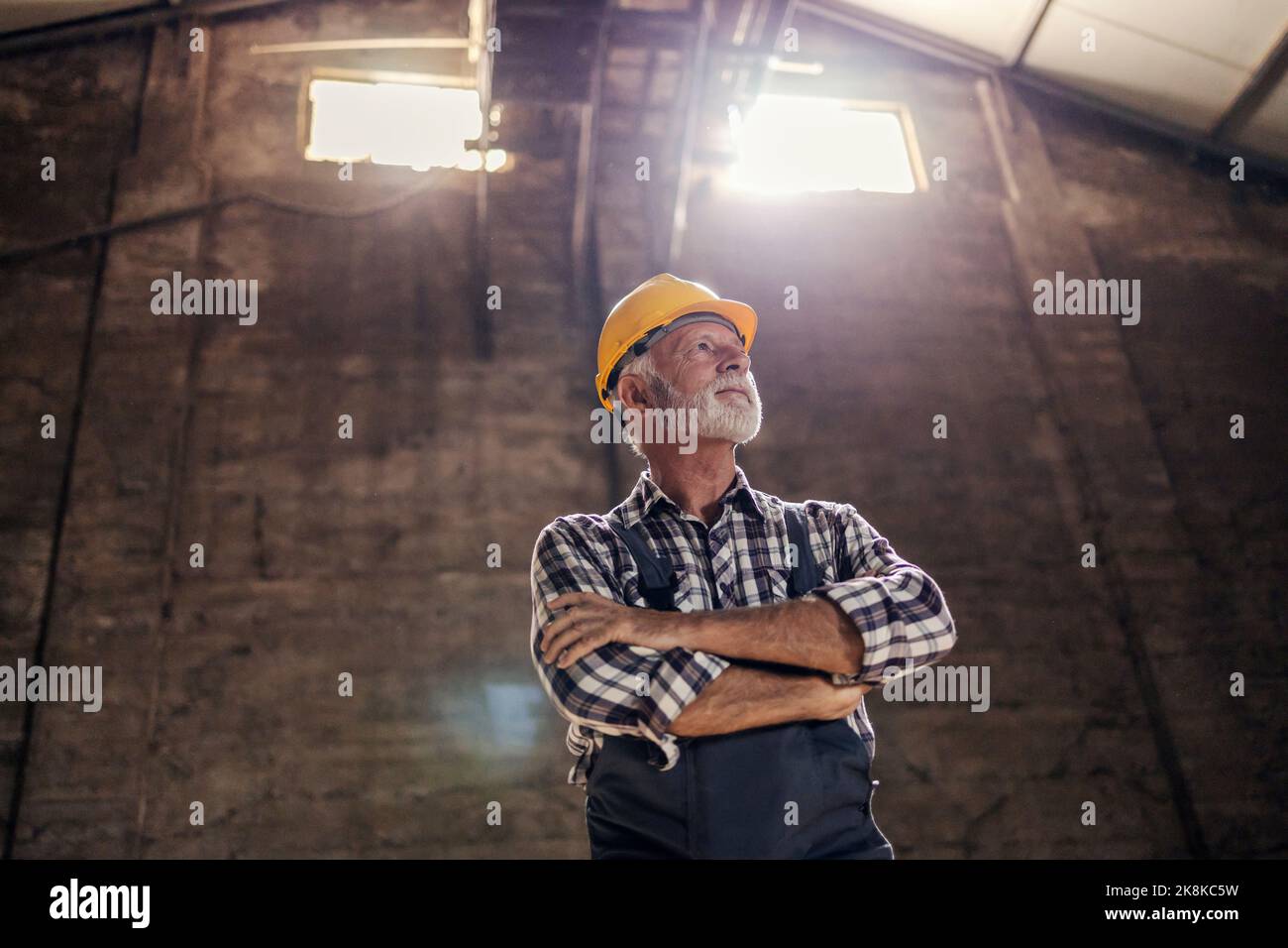 Vue à angle bas d'un ancien travailleur à barbe blanche avec les mains croisées en attendant la prochaine tâche dans l'usine. Banque D'Images