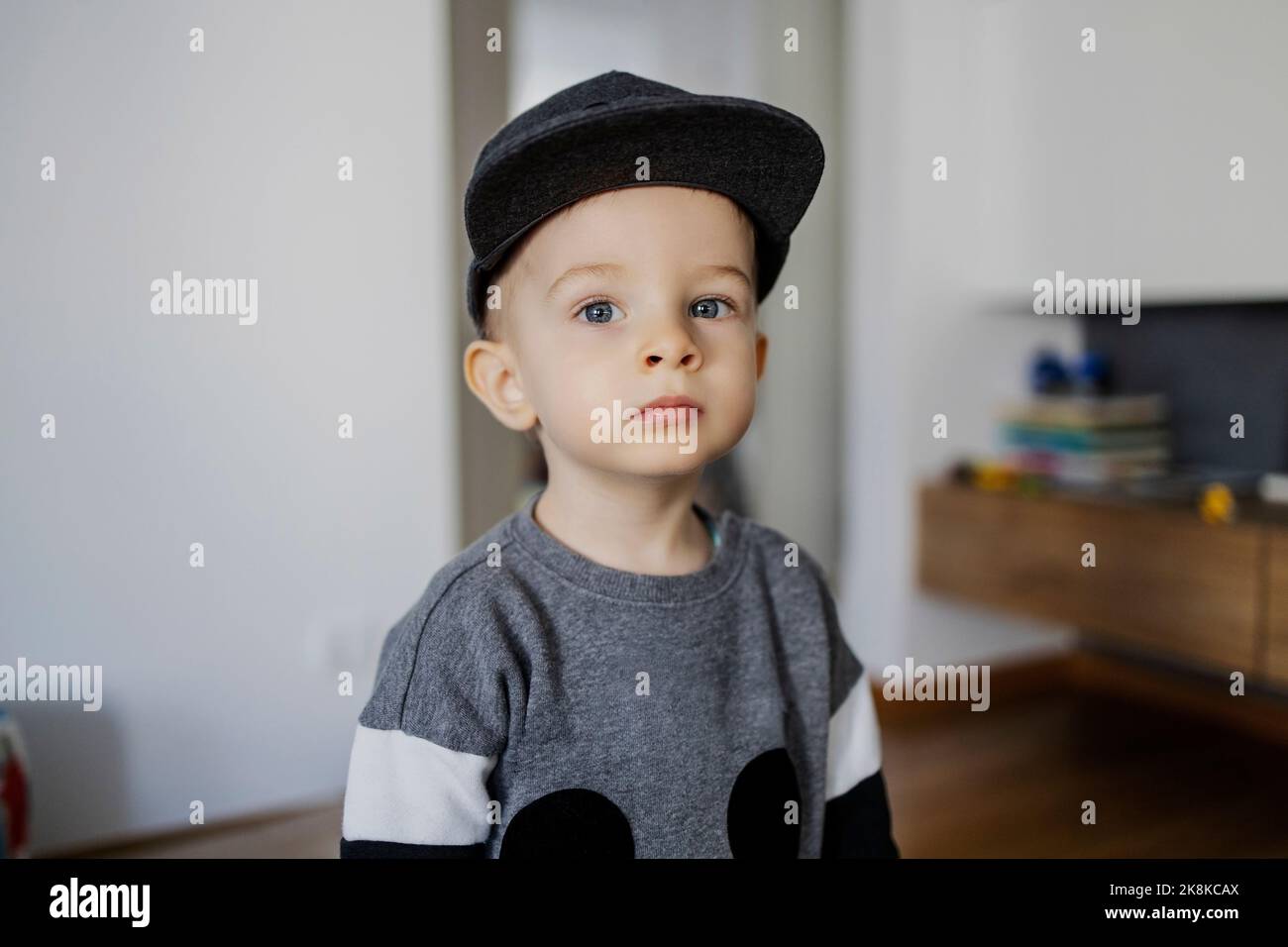 Portrait d'un bébé garçon. Un mignon petit garçon dans un sweat-shirt et un chapeau est regarder depuis l'espace intérieur latéral de la maison. Le garçon a un visage vague Banque D'Images