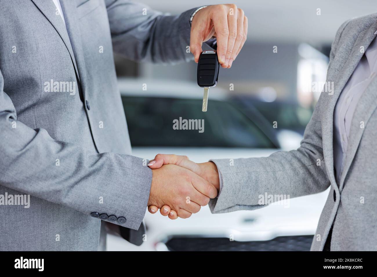 Gros plan d'un vendeur de voiture qui se secoue la main avec le client et lui remet les clés de sa voiture tout en se tenant dans un salon de voiture. Banque D'Images