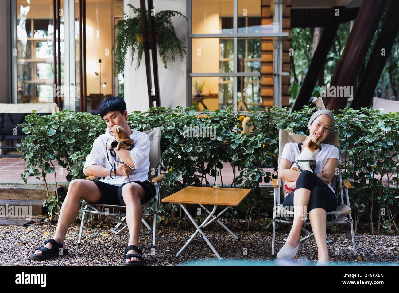 Un couple asiatique tenant un petit chien assis sur une chaise dans le jardin à l'extérieur. Banque D'Images