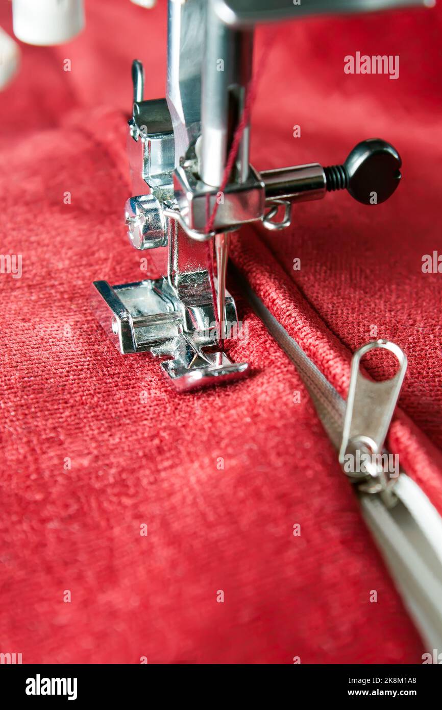 Machine à coudre moderne avec des ragoûts de pied de presse spéciaux sur la fermeture éclair sur l'article rouge de vêtements. Processus de couture Banque D'Images