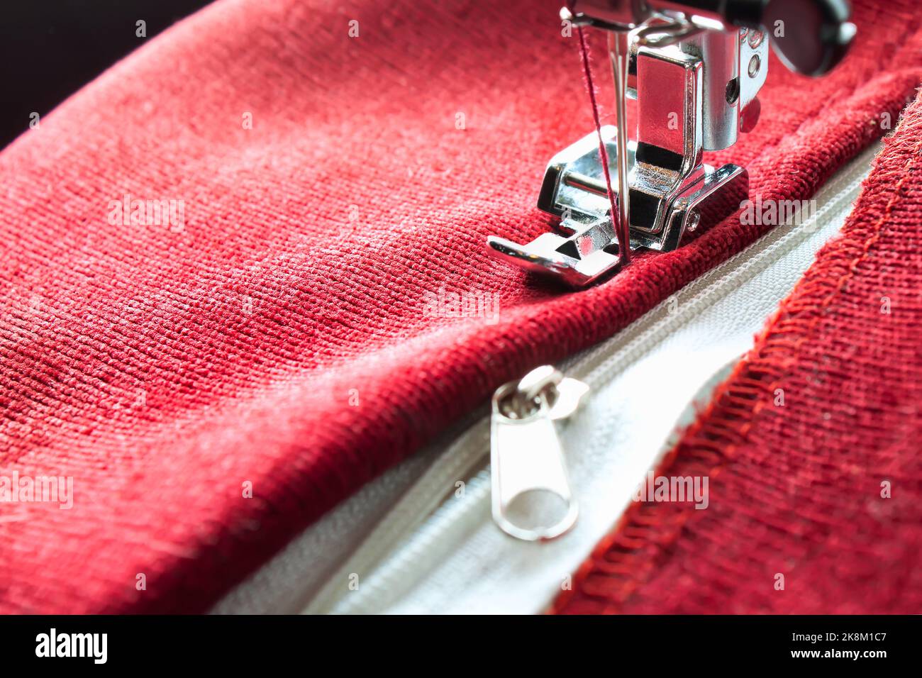 Machine à coudre moderne avec des ragoûts de pied de presse spéciaux sur la fermeture éclair sur l'article rouge de vêtements. Processus de couture Banque D'Images