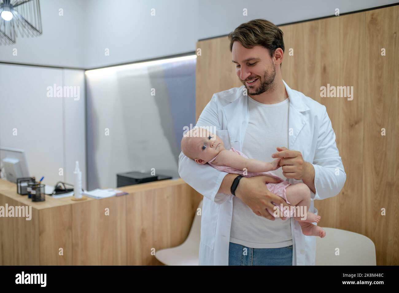 Jeune pédiatre gai vérifiant les réflexes d'un nouveau-né Banque D'Images