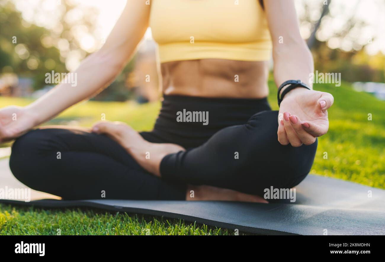 Femme sportive méconnue assise en position lotus sur un tapis de fitness méditant à l'extérieur, détente dans la nature. Détente et tranquillité d'esprit. Harmonie Banque D'Images