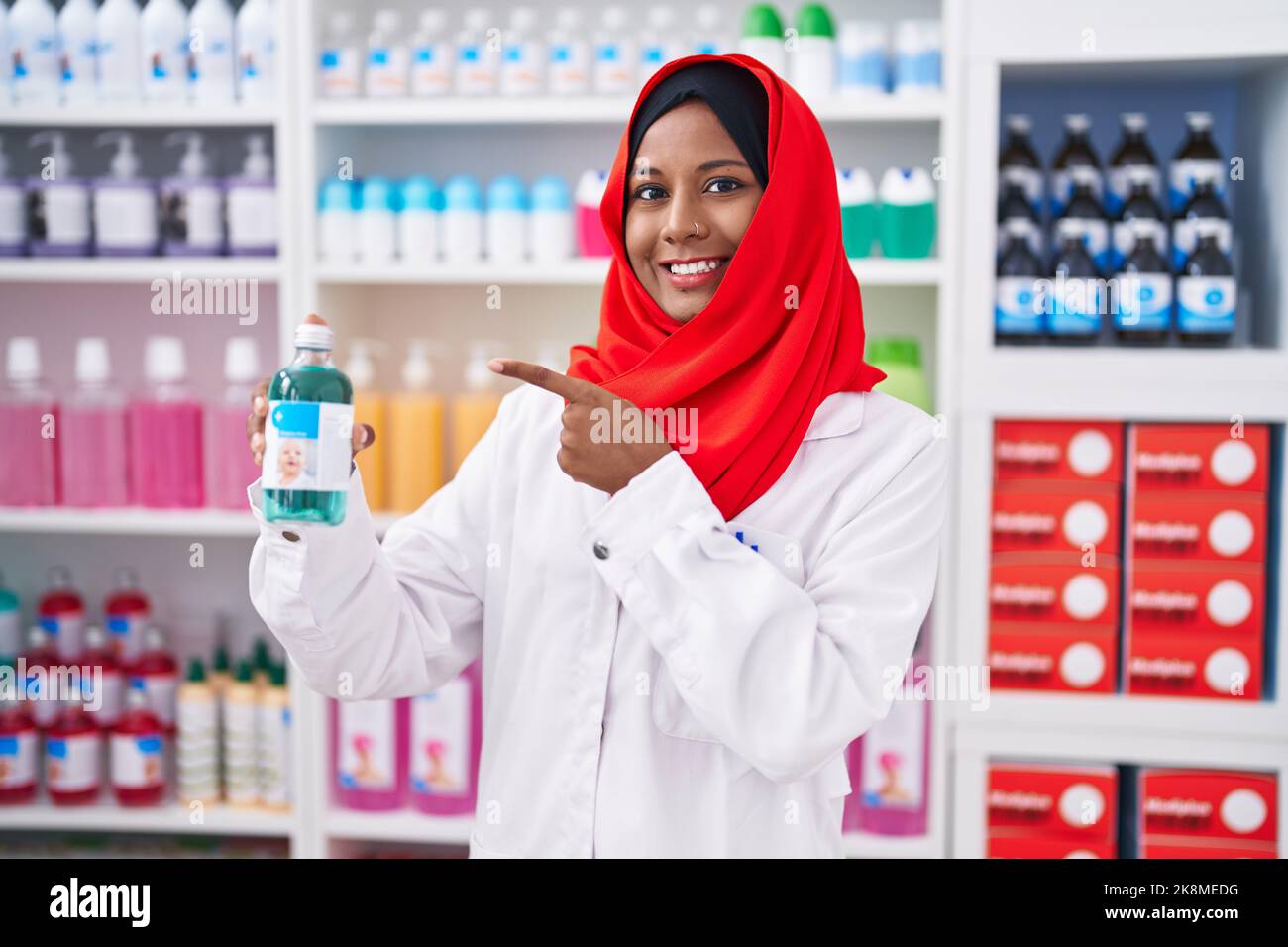 Jeune femme arabe travaillant à pharmacie pharmacie pharmacie tenue sirop sourire heureux pointant avec la main et le doigt Banque D'Images