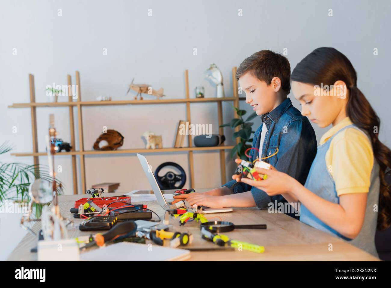 préteen garçon en utilisant un ordinateur portable près de fille tenant une partie mécanique du modèle robotique, image de stock Banque D'Images