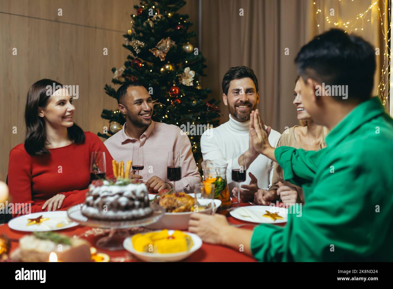 Dîner de Noël festif, plusieurs amis en visite assis à la table se reposant et riant, célébrant le nouvel an ensemble groupe d'hommes et de femmes. Banque D'Images