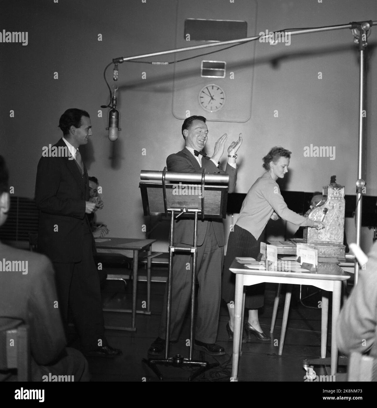 Oslo 19541209 du programme ​​radio de NRK "l'heure de la lumière" où le concours de connaissances "la question" avec Rolf Kirkvaag a été inclus. La caisse « Jonatan » était au centre du programme. Les questions devaient être trouvées sur les questions, elles étaient divisées en cinq groupes après des élections libres. Cinq couronnes pour la première droite, en montant à quatre-vingt couronnes brillantes si vous avez répondu correctement à toutes les questions, c'était le concept derrière la question. Ici, un sourire Kirkvaag applaudit une bonne réponse, tandis qu'un assistant sert la caisse Jonatan pour payer les gains. Photo: NTB / NTB Banque D'Images