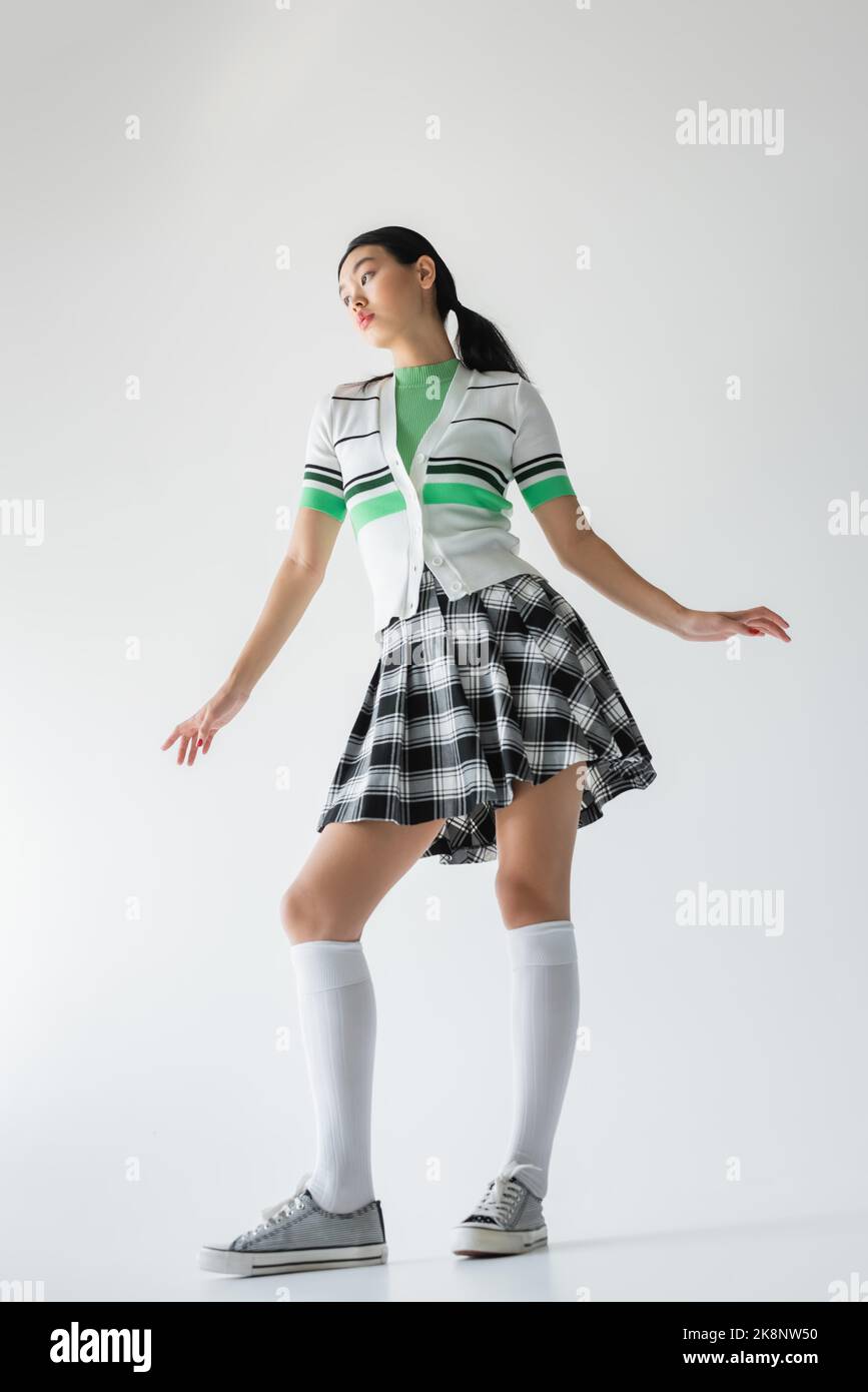 Vue à angle bas du modèle asiatique tendance en chaussettes et jupe de genou posé sur fond gris Banque D'Images