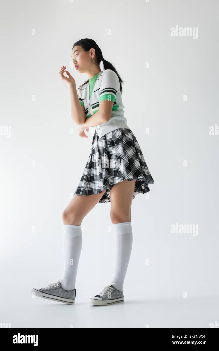 Vue basse de la jeune femme asiatique dans les chaussettes de genou regardant loin sur fond gris Banque D'Images