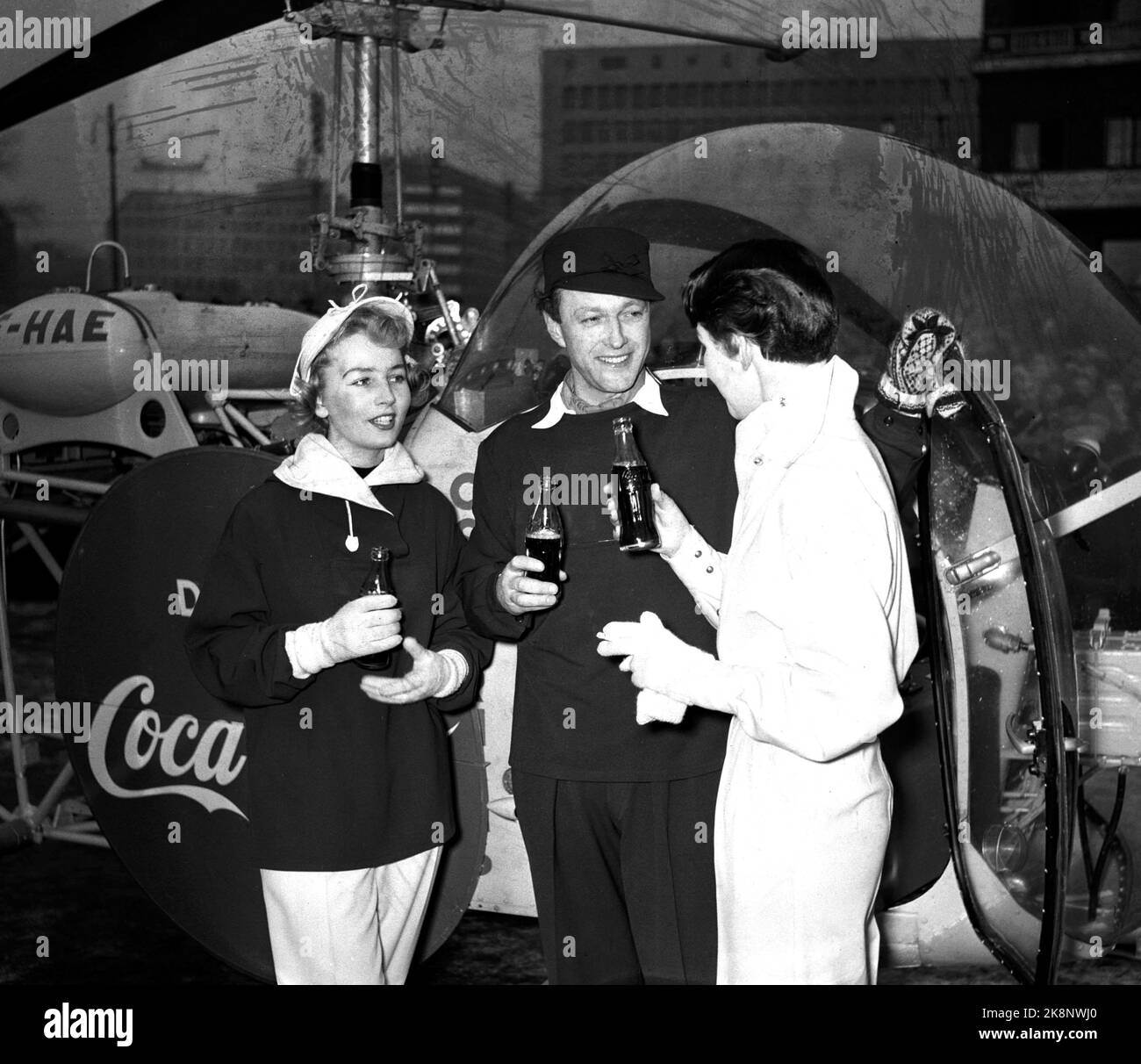 Jeux olympiques d'hiver d'Oslo 1952. Pendant les Jeux Olympiques, Coca Cola a eu une grande campagne publicitaire. Dans la photo, nous voyons un hélicoptère avec la publicité Coca Cola qui a atterri devant la mairie. Ici, les gens aiment boire du Coca Cola directement de la bouteille. Banque D'Images