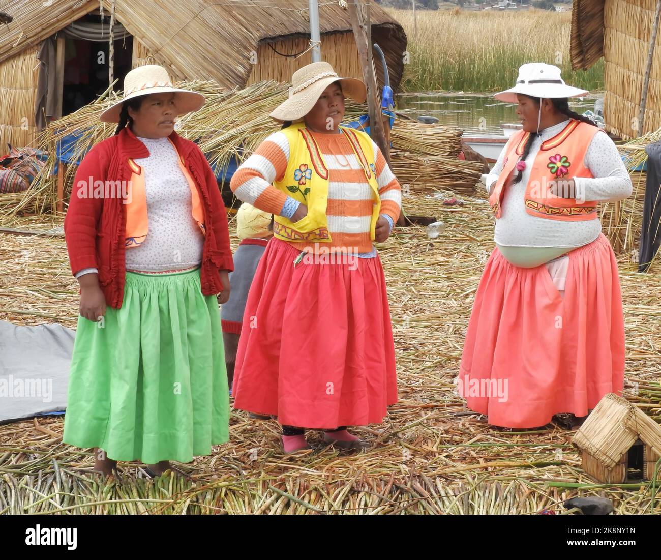 Femmes autochtones debout près de maisons de paille dans les îles flottantes d'Uros dans le lac Titicaca au Pérou Banque D'Images