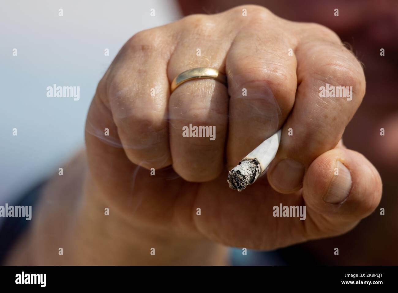 Une cigarette allumée avec fumée de cigarette dans une main masculine, provoquant une dépendance et dangereuse pour la santé Banque D'Images