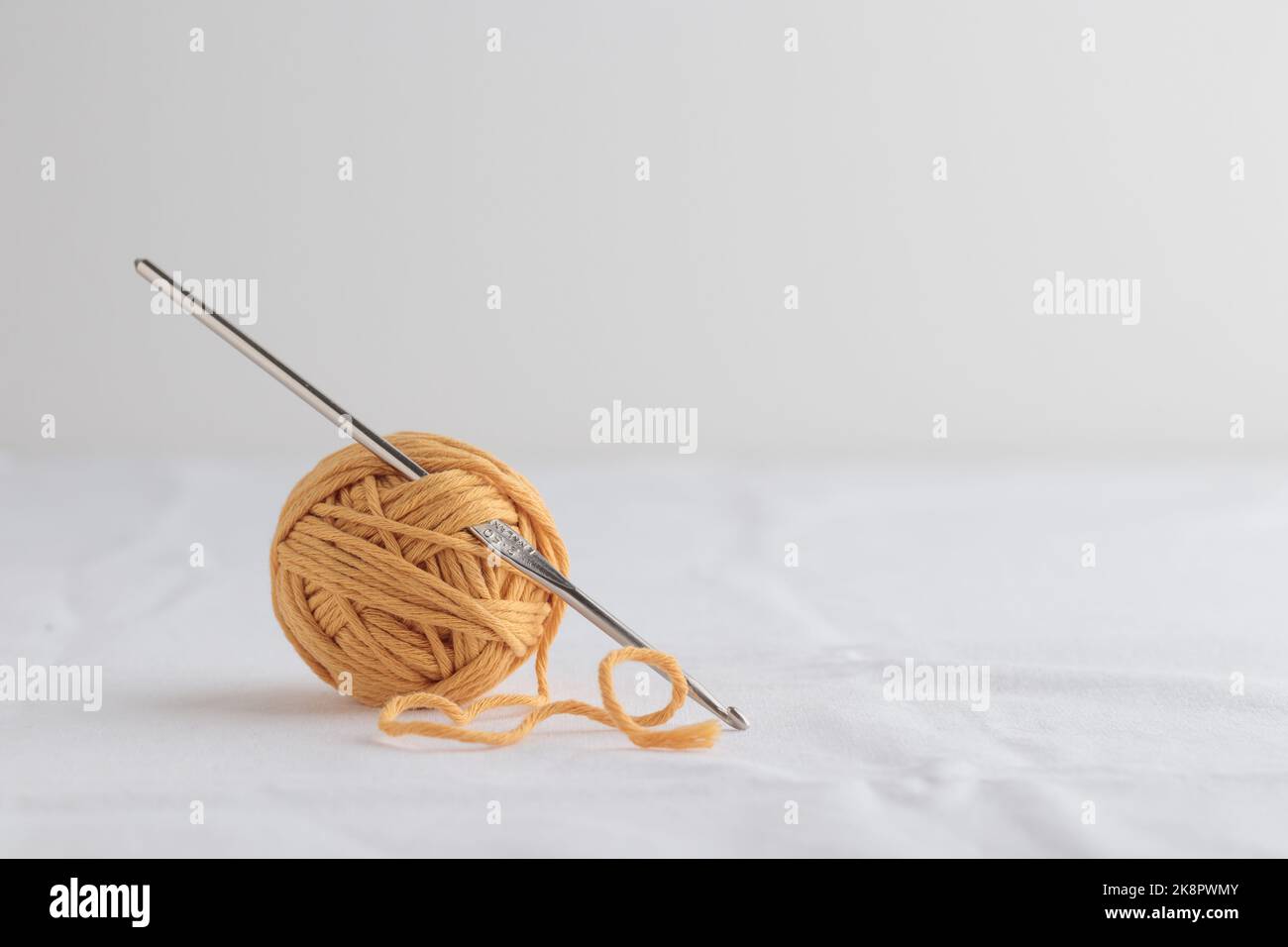 Crochet en crochet et une petite boule de fil jaune sur fond blanc Banque D'Images