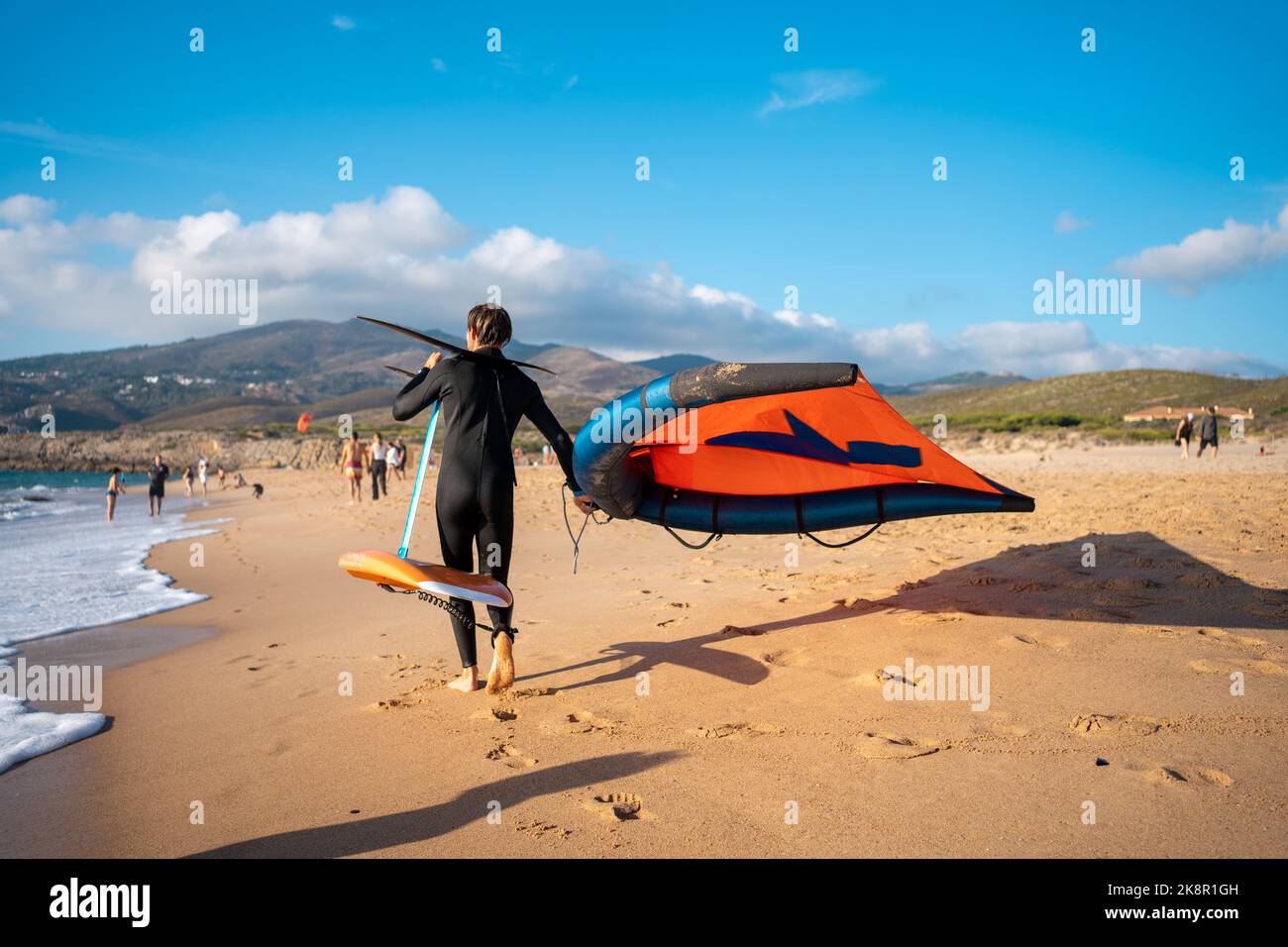 Surfeur sur papier d'aluminium surfant sur l'hydroglisseur dans la mer par une journée ensoleillée. Homme avec équipement d'hydroptère de cerf-volant marche plage de sable Banque D'Images