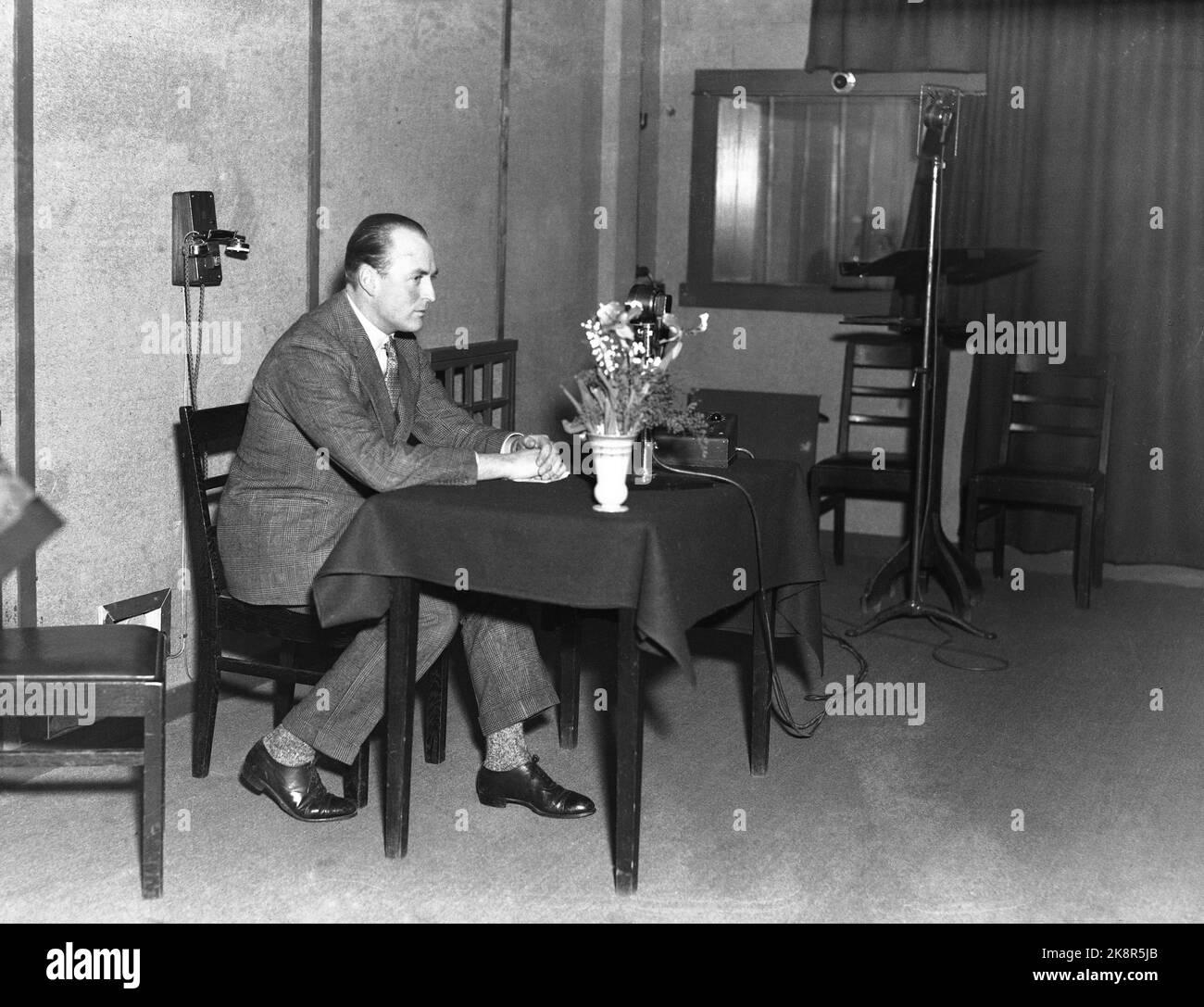 Oslo 19331205 le prince héritier Olav parle à la radio NRK. Le prince héritier en studio, assis à une petite table, microphone et bouquet de fleurs sur la table, téléphone sur le mur en arrière-plan. Photo: NTB / NTB Banque D'Images