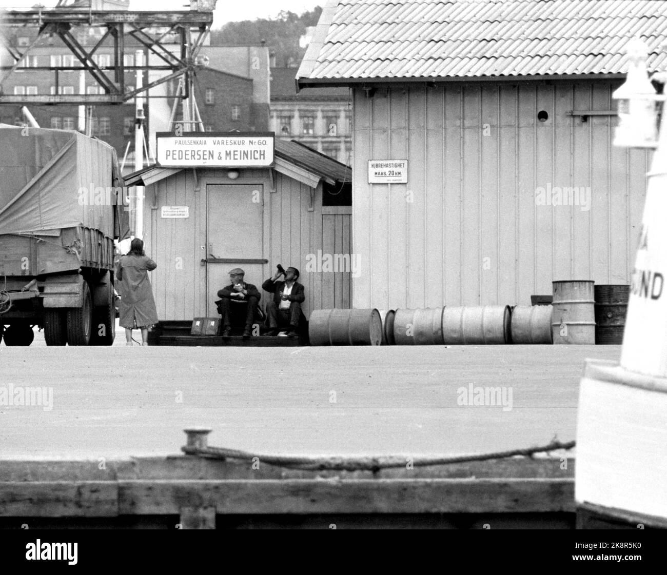 Oslo à l'été 1962. Une promenade le long de l'Akerselva de OS à OS. Au hangar n° 60 de Pedersen et Meinich sur le quai à 'Køla-Pålsen' (officiellement Paulsenkaia), deux travailleurs ont trouvé un endroit où ils peuvent manger la boîte à lunch et partager une bouteille, et ils sont heureux de partager une dame qui passe aussi .. Photo: Åge Storløkken / actuel / NTB. Lok physique: Actuel 1962 No. 37: Akerselva, vous avez vieux vous gris. Banque D'Images