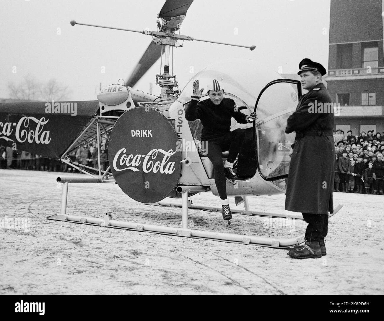 Jeux olympiques d'hiver d'Oslo 1952. Pendant les Jeux Olympiques, Coca Cola a eu une grande campagne publicitaire. Dans la photo, nous voyons un hélicoptère avec la publicité Coca Cola qui atterrit devant la mairie. Un patineur se lève. Banque D'Images