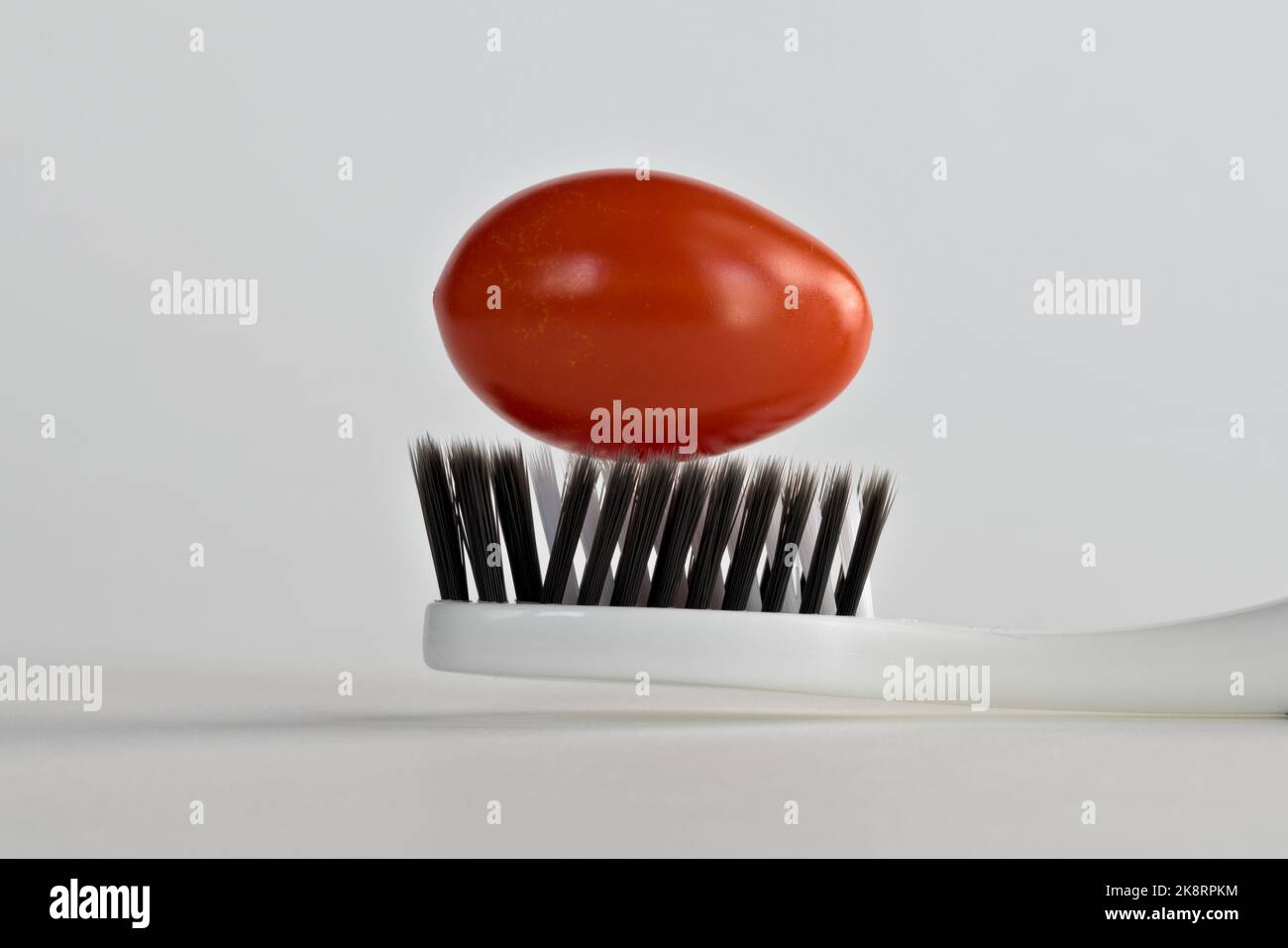 une tomate roma cerise sur une brosse à dents noire et blanche Banque D'Images