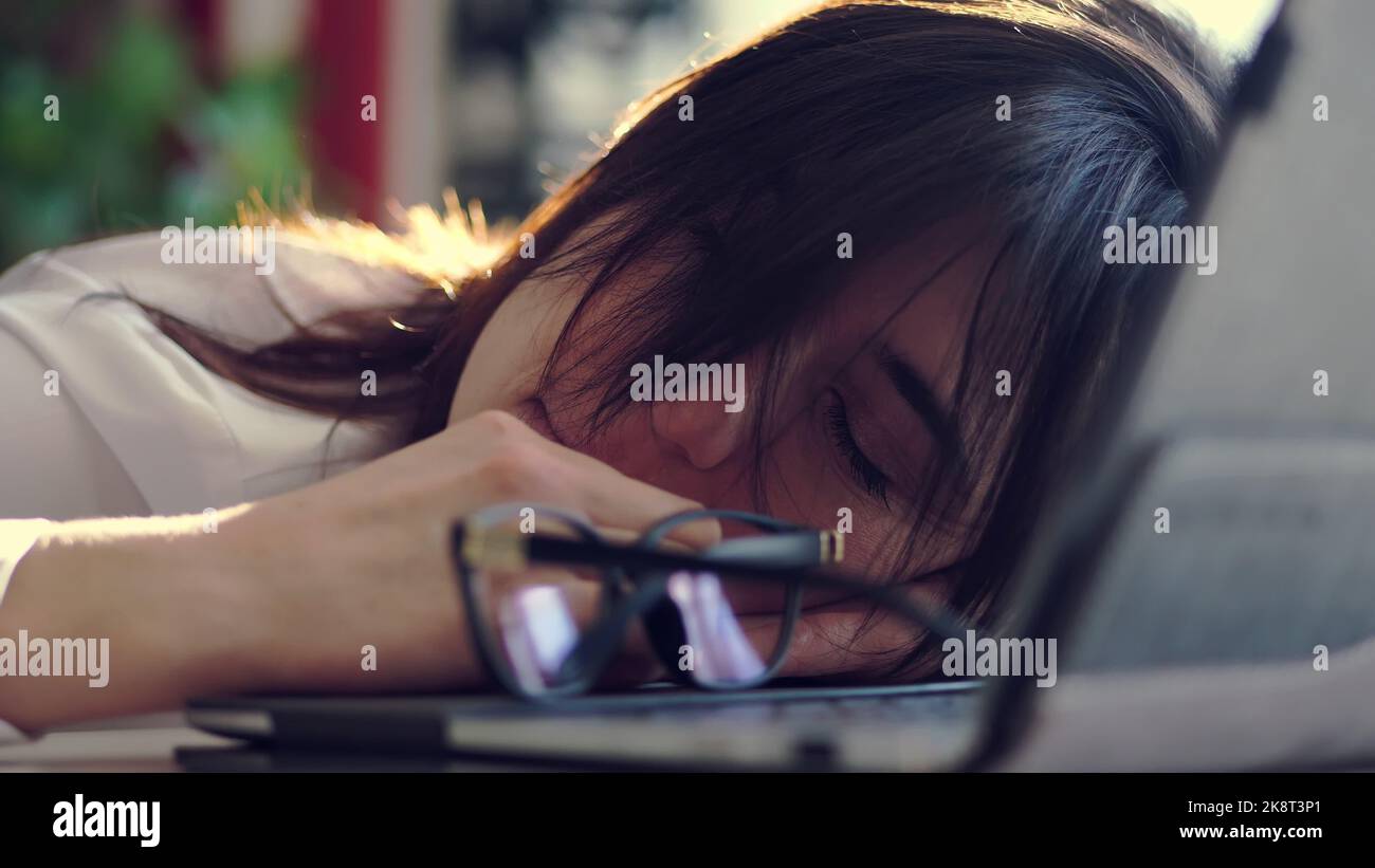 Une jeune femme d'affaires surchargée, épuisée et fatiguée retire des lunettes, se reposant, dormant au-dessus d'un ordinateur portable dans un bureau de son bureau. Elle est submergée par le travail, portrait tourné. Photo de haute qualité Banque D'Images