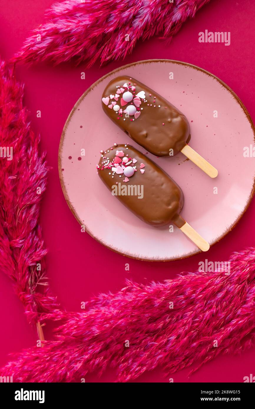Crème glacée à base de cupcake et crème au chocolat. Petits gâteaux au chocolat sur une assiette rose avec fleurs séchées roses sur un fond de fuchsia brillant. Vue d'en haut Banque D'Images