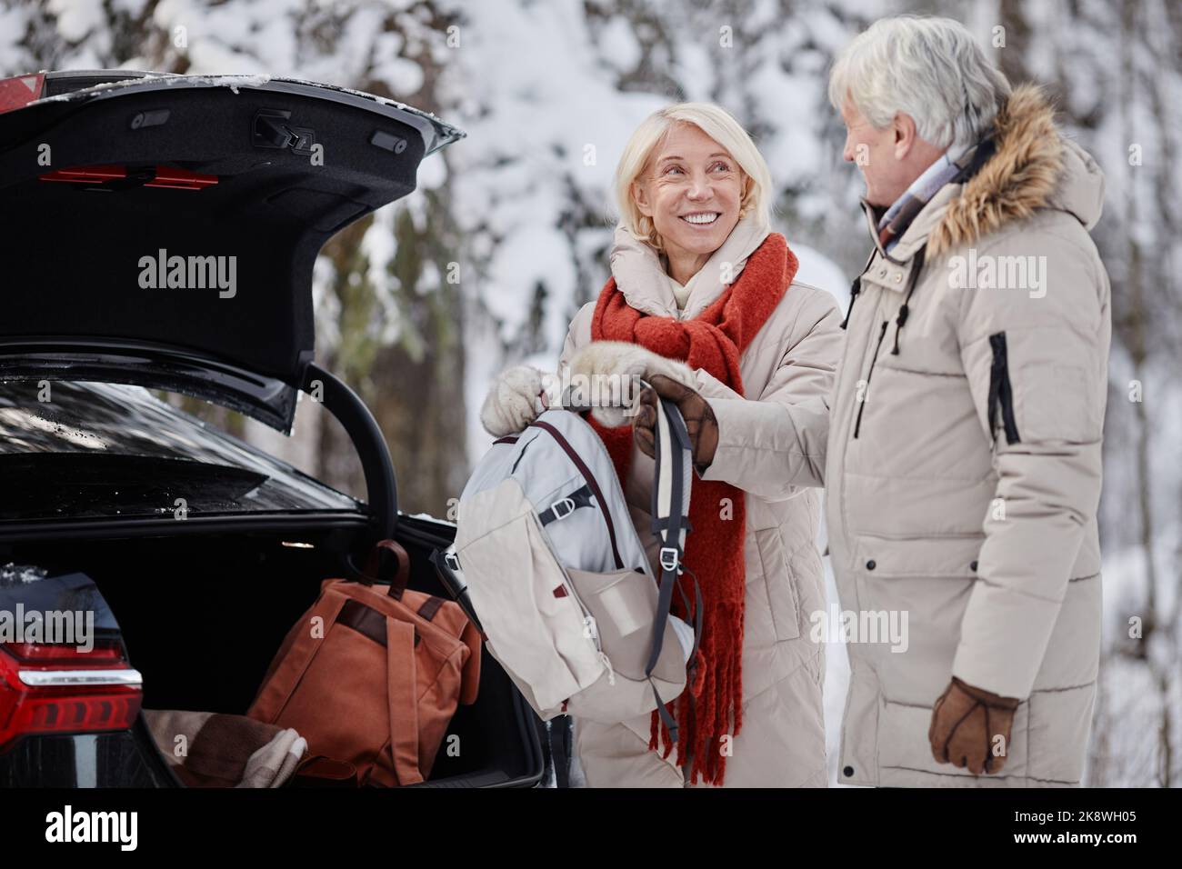 Vue latérale portrait d'un couple senior souriant ouvrant le coffre de voiture tout en appréciant une escapade hivernale dans la nature ensemble, espace de copie Banque D'Images