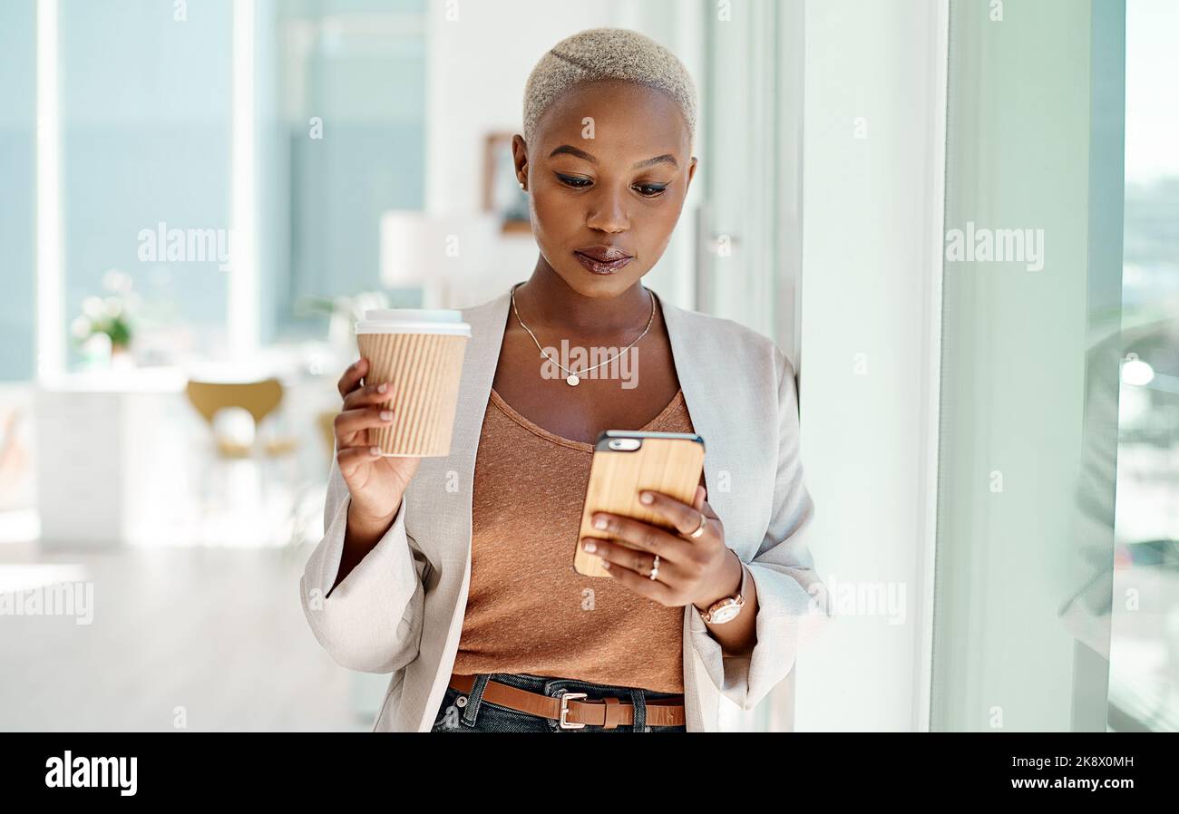 Shes un pro de la gestion des affaires en déplacement. Une jeune femme d'affaires utilisant un téléphone portable tout en buvant du café dans un bureau. Banque D'Images