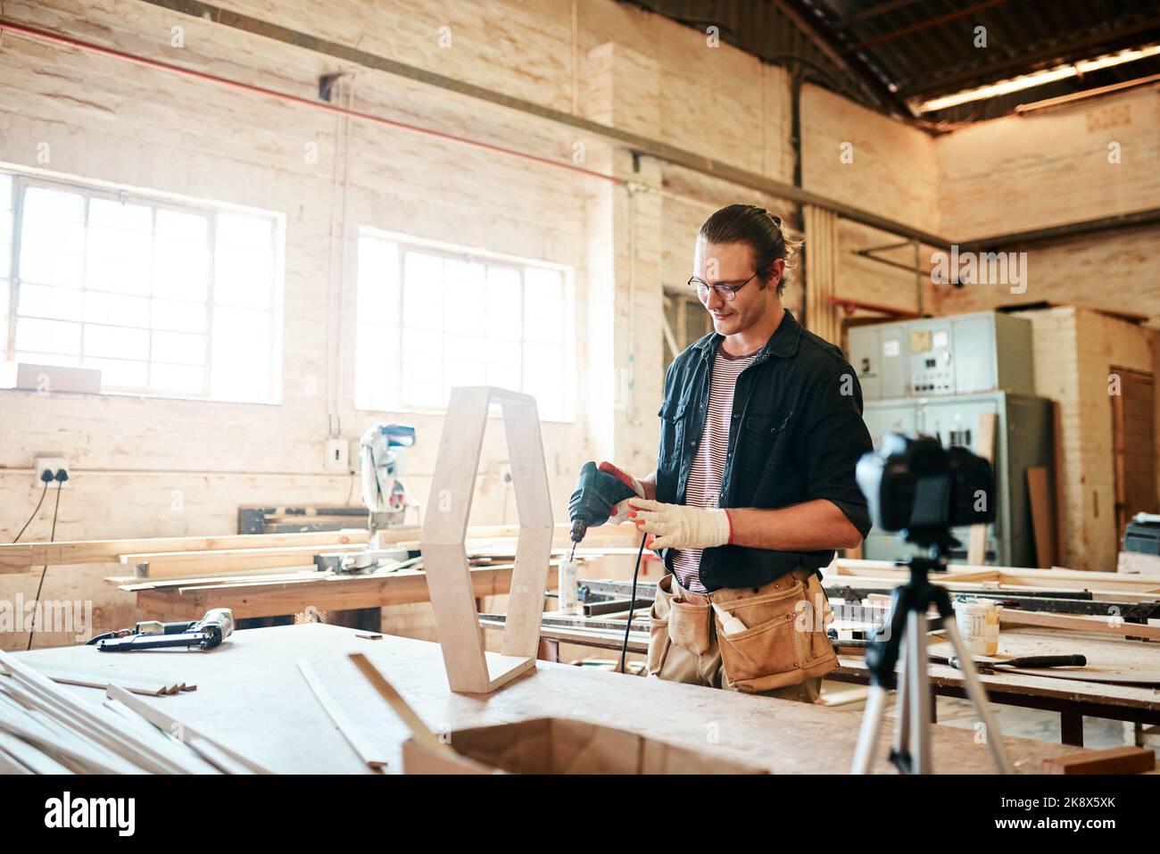 Toujours jouer en toute sécurité quand vous travaillez avec des gars d'outils électriques. Jeune menuisier enregistrer un tutoriel de lui faire un chef-d'œuvre en bois sur une caméra vidéo Banque D'Images