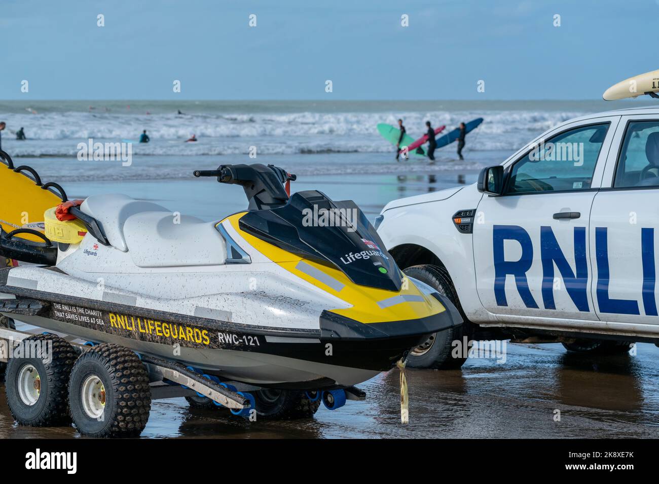 Un véhicule et un scooter des mers RNLI à Croyde Bay, North Devon, Royaume-Uni, avec des surfeurs qui pénètrent dans l'eau en arrière-plan. Banque D'Images