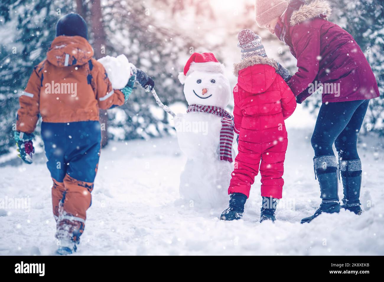 Famille qui garde un adorable bonhomme de neige dans le parc enneigé. Banque D'Images