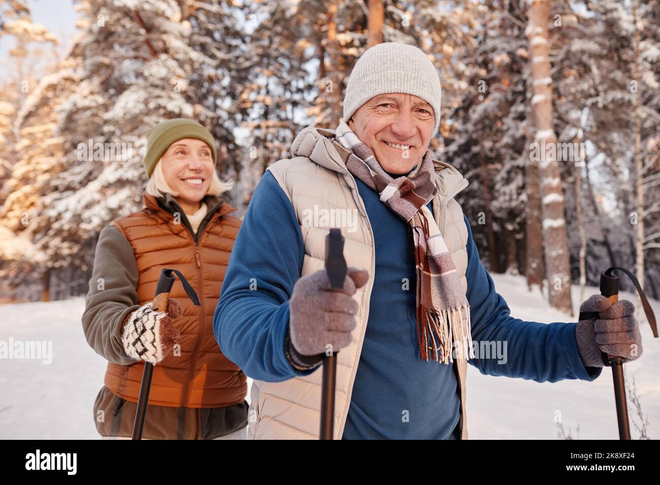 Portrait à la taille du couple senior heureux marchant avec des bâtons dans la forêt d'hiver et souriant à la caméra Banque D'Images