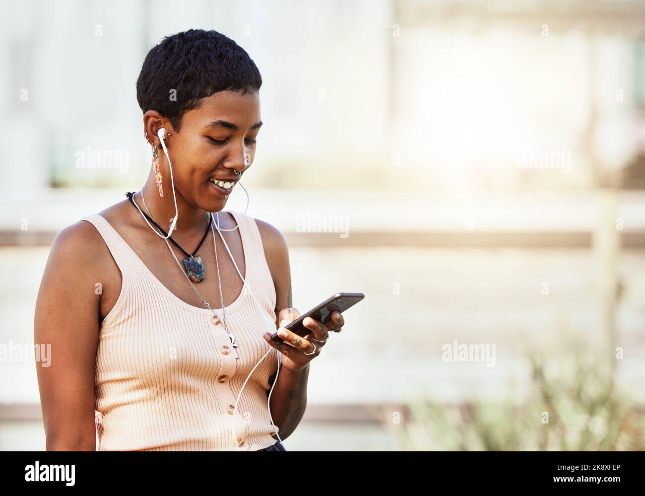 Femme noire, sourire et smartphone avec écouteurs, musique et communication, réseaux sociaux et diffusion audio en ligne. Africain américain, à l'écoute Banque D'Images