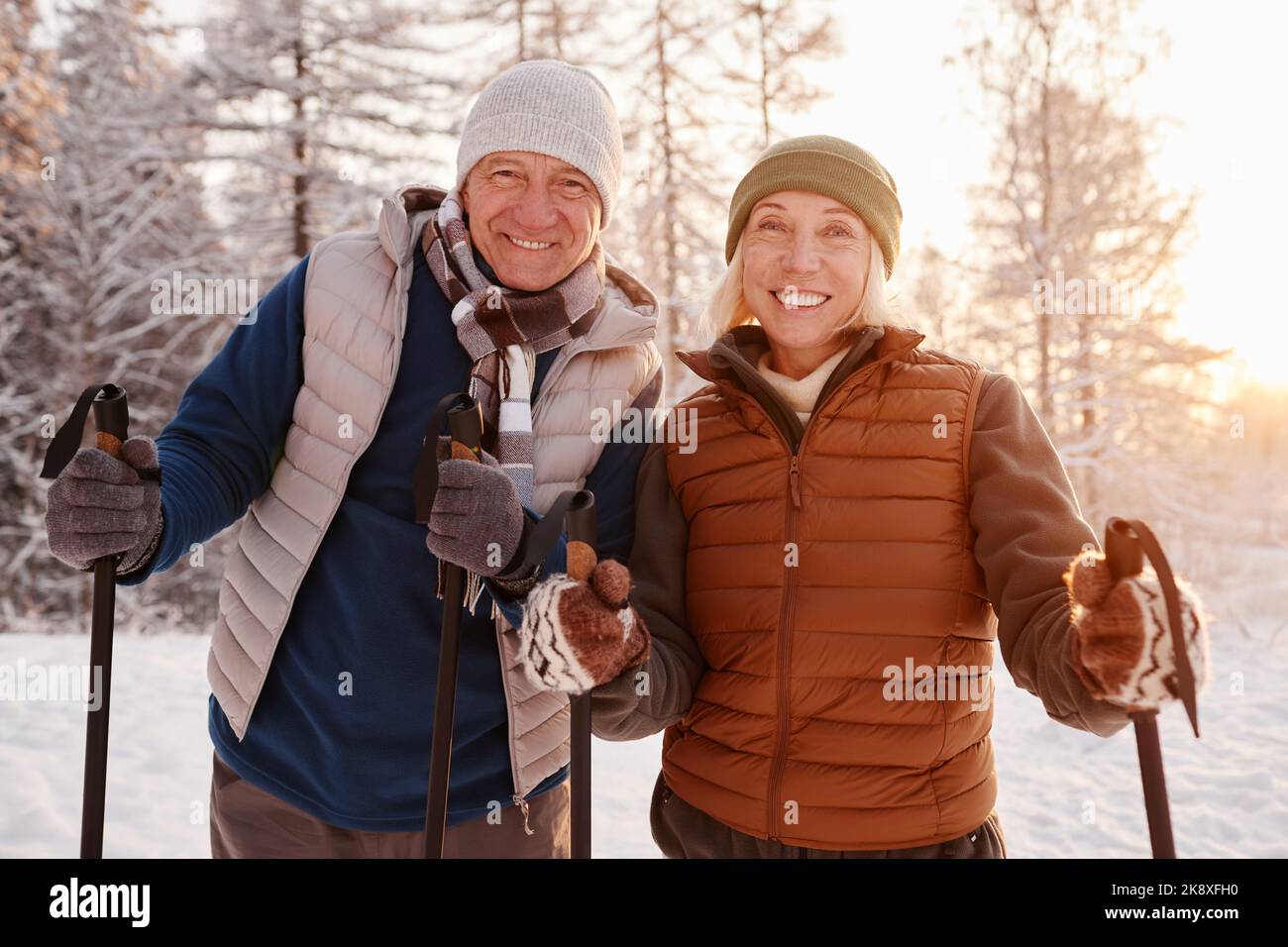 Portrait à la taille du couple senior actif en train de profiter de la marche nordique avec des bâtons dans la forêt d'hiver et de regarder l'appareil photo Banque D'Images