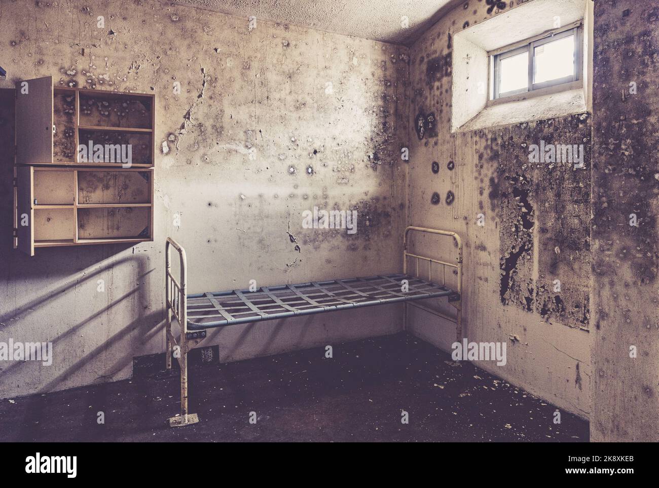 Un cadre de lit en métal et un casier de rangement dans une cellule de détenus dans une prison anglaise désutilisée. Banque D'Images