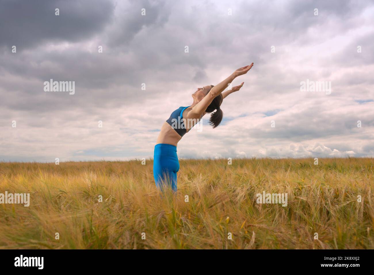 Femme s'exerçant et faisant un étirement au milieu d'un champ. Entraînez-vous en plein air. Banque D'Images