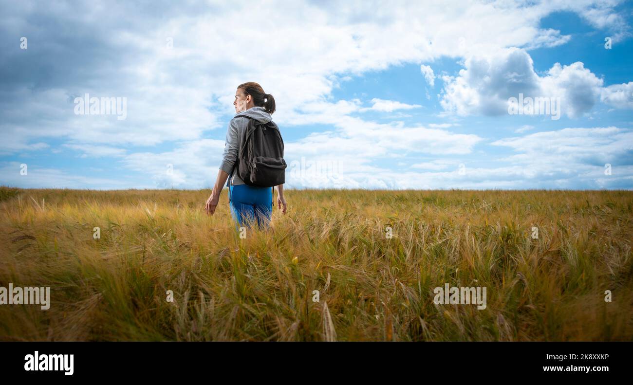 Femme avec un sac à dos marchant dans un champ, appréciant la campagne. Banque D'Images