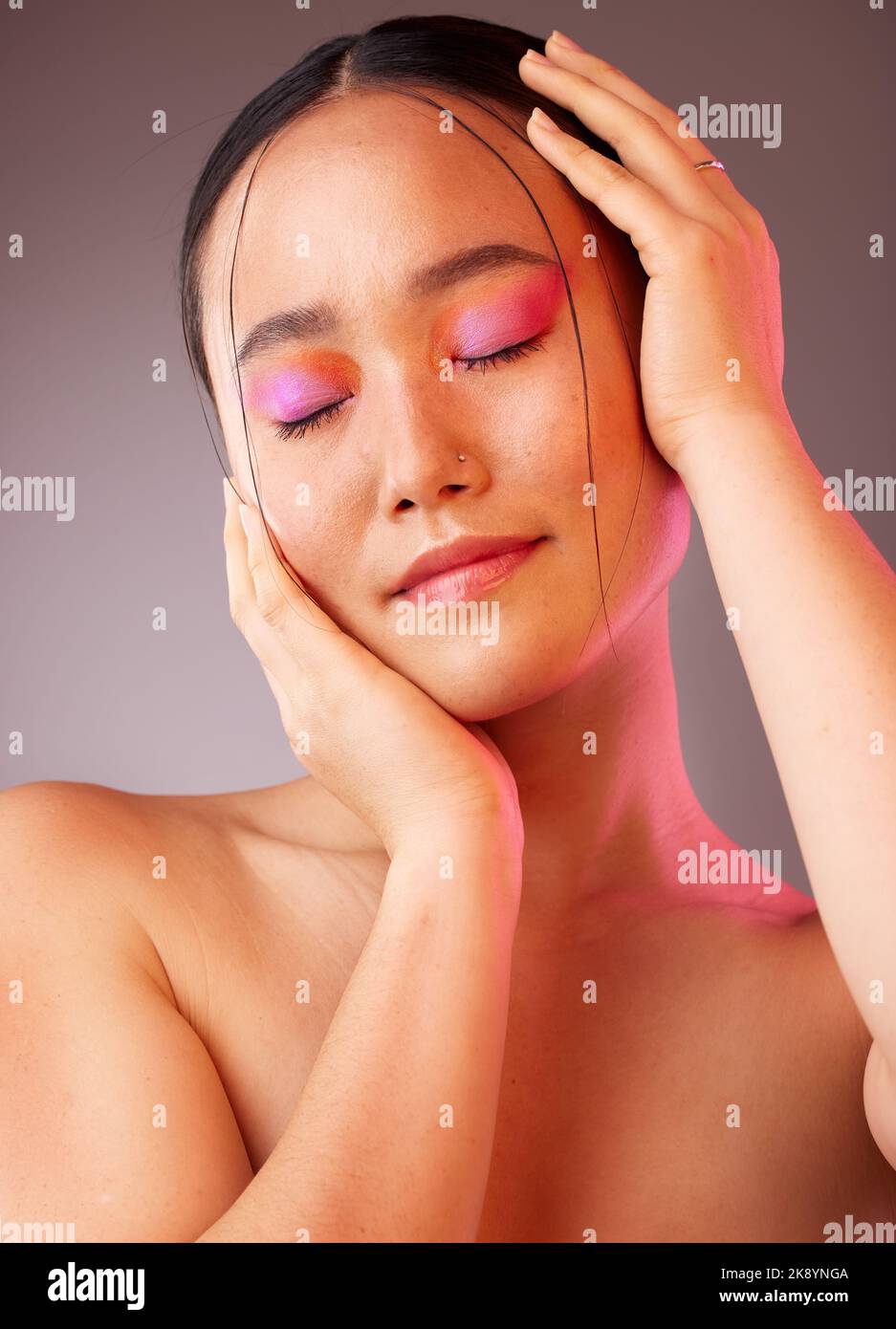 Fard à paupières, femme asiatique et de beauté avec les mains sur le visage pose avec des cosmétiques roses et orange. Modèle de maquillage tendance et coloré pour Gen Z Banque D'Images