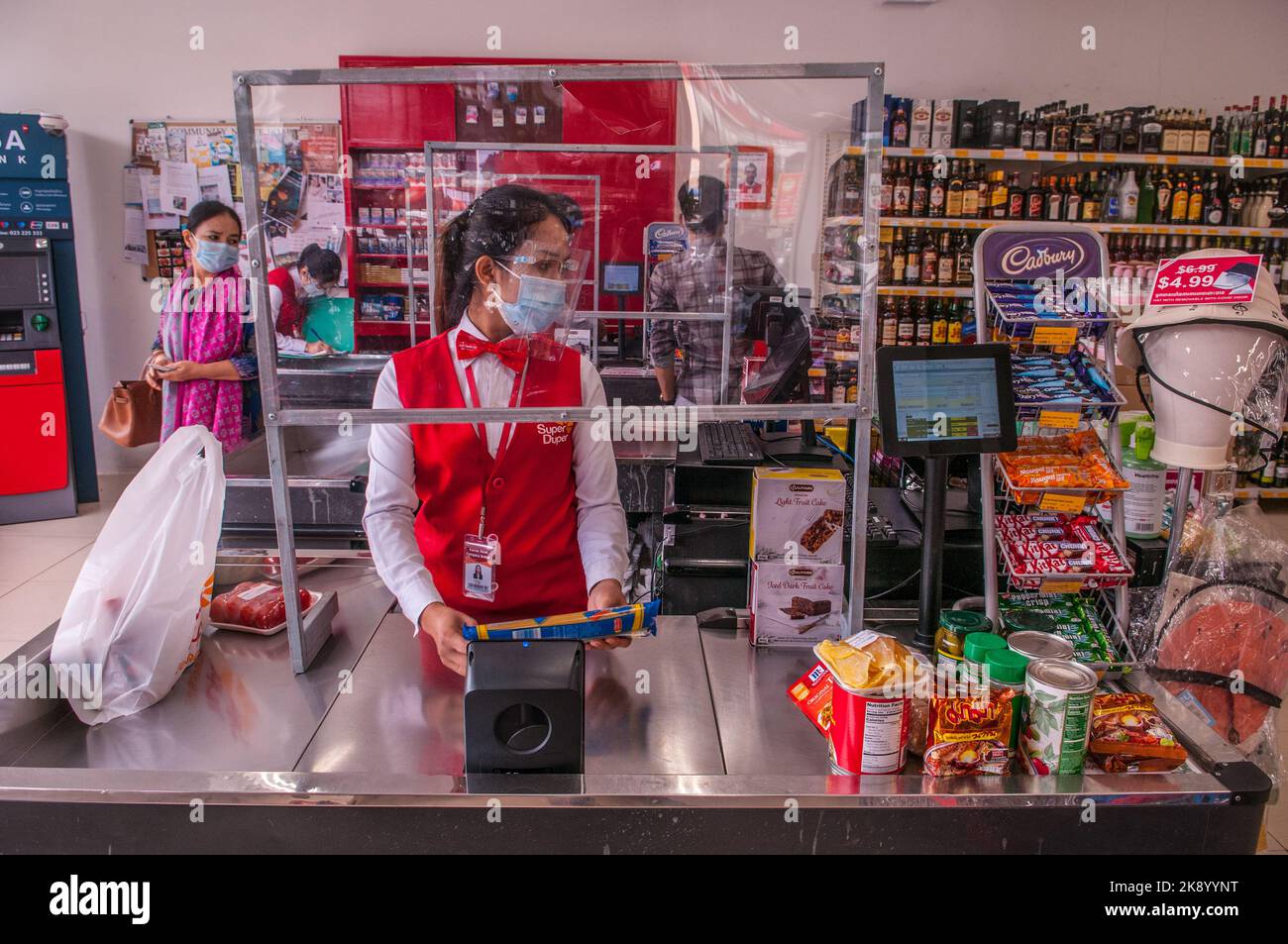 En raison d'une épidémie de COVID - 19, un caissier de supermarché, à un comptoir de caisse, porte un écran facial de protection. Phnom Penh, Cambodge. © Kraig Lieb Banque D'Images