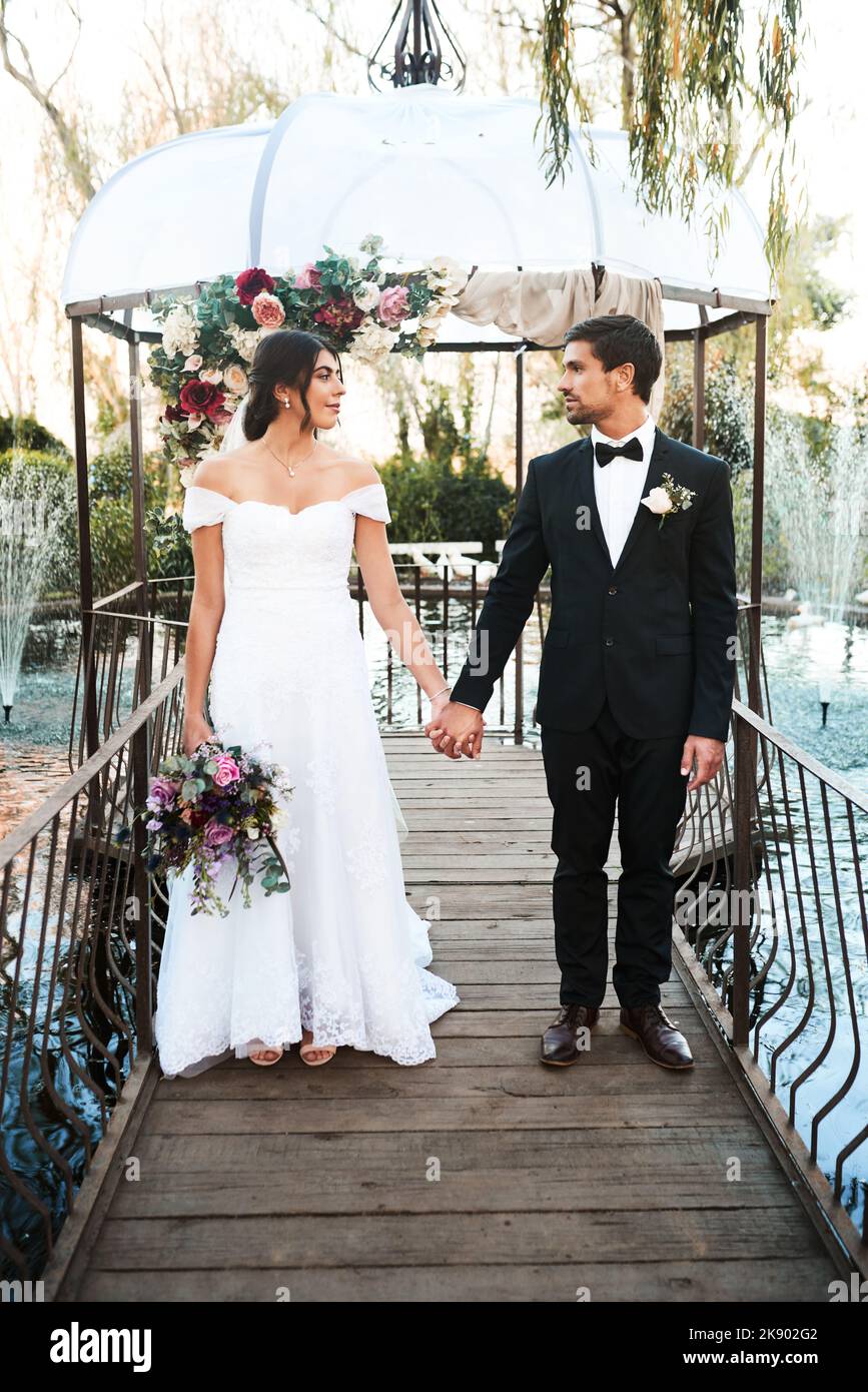 Ils marchaient pour toujours ensemble. Prise de vue en longueur d'un jeune couple heureux, récemment mariés, qui tient les mains ensemble à l'extérieur le jour de leur mariage. Banque D'Images