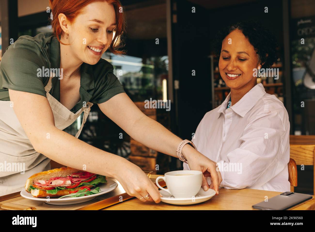 Une jeune serveuse heureuse servant un sandwich et une tasse de café à un client dans un café moderne. Jeune femme joyeuse travaillant dans un restaurant de restauration rapide. Banque D'Images