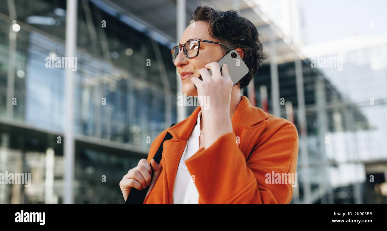Femme d'affaires mature parlant au téléphone tout en se rendant au travail en ville. Femme d'affaires qui fait des plans pour la journée tout en marchant à son bureau Banque D'Images