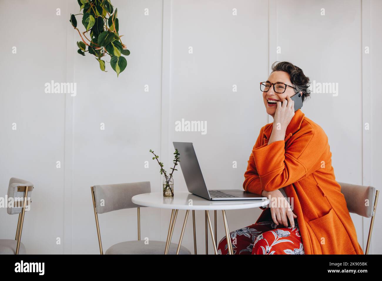 Bonne femme d'affaires mûre parlant sur un appel téléphonique tout en travaillant à distance. Femme d'affaires réussie souriant gaiement pendant un appel téléphonique discussio Banque D'Images
