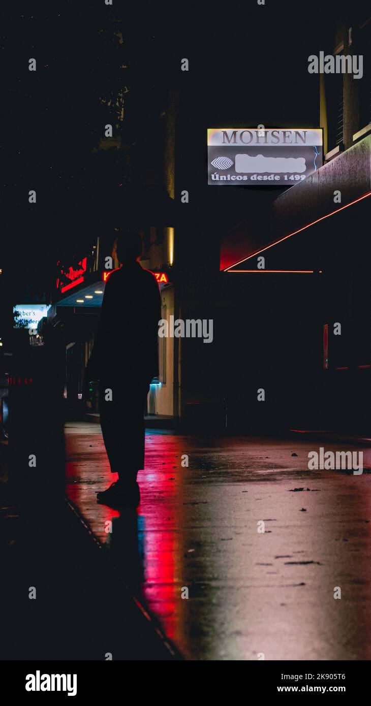 La vie nocturne dans les rues. Des panneaux lumineux au néon se reflètent sur la rue humide/pluvieuse. Enseignes au néon créant la silhouette d'une personne. Banque D'Images