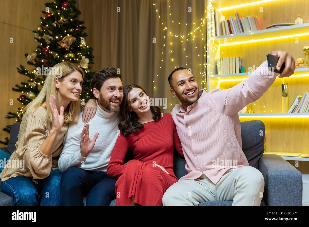 La fête du nouvel an accueille divers groupes d'amis, d'hommes et de femmes, assis sur le canapé, emportant un selfie ensemble, utilisant un smartphone, les clients regardant le téléphone, parlant sur un appel vidéo pour Noël Banque D'Images