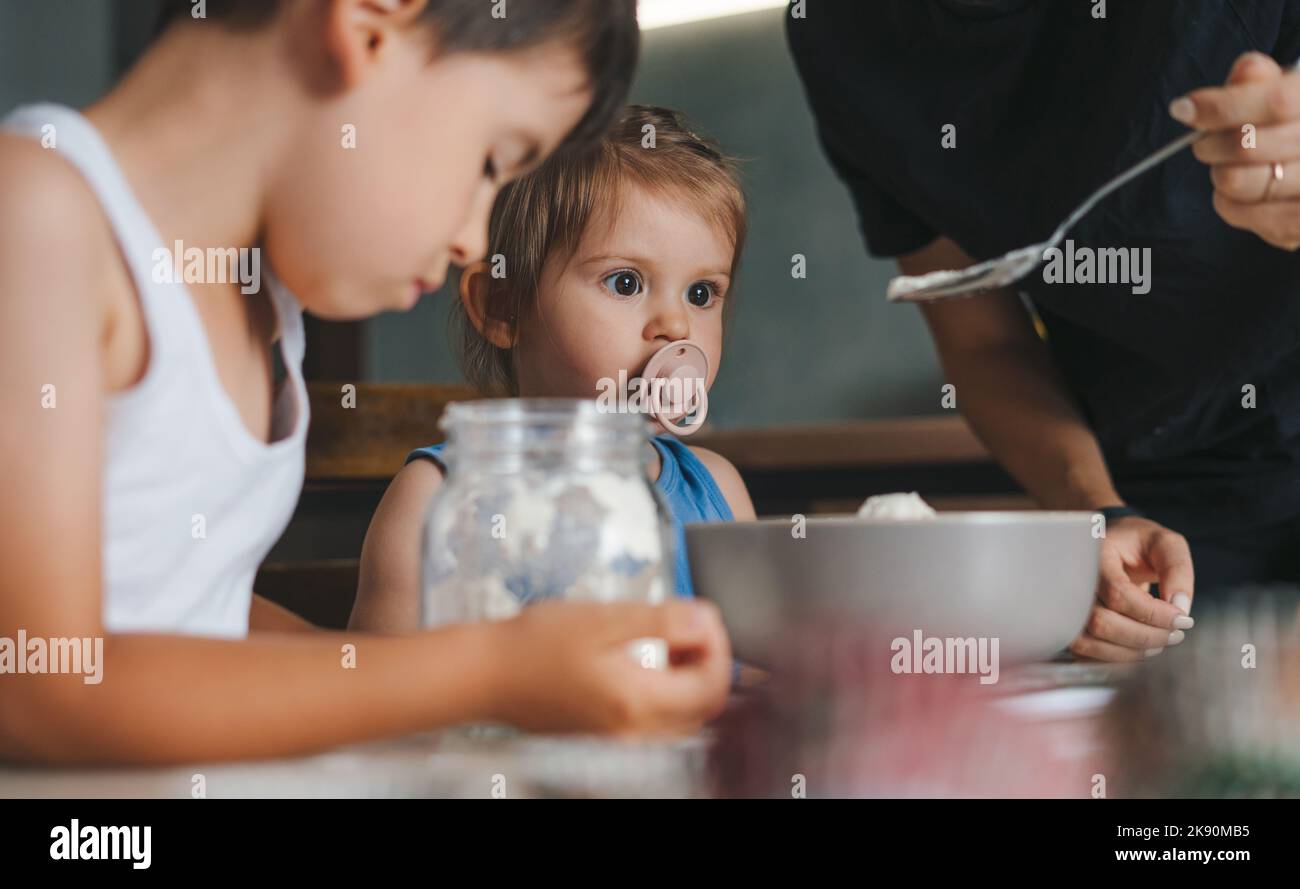 Deux enfants du caucase aidant sa mère qui pèse de la farine dans la cuisine. Concept d'activité familiale. Concept « Love People ». Bonne famille, enfance Banque D'Images