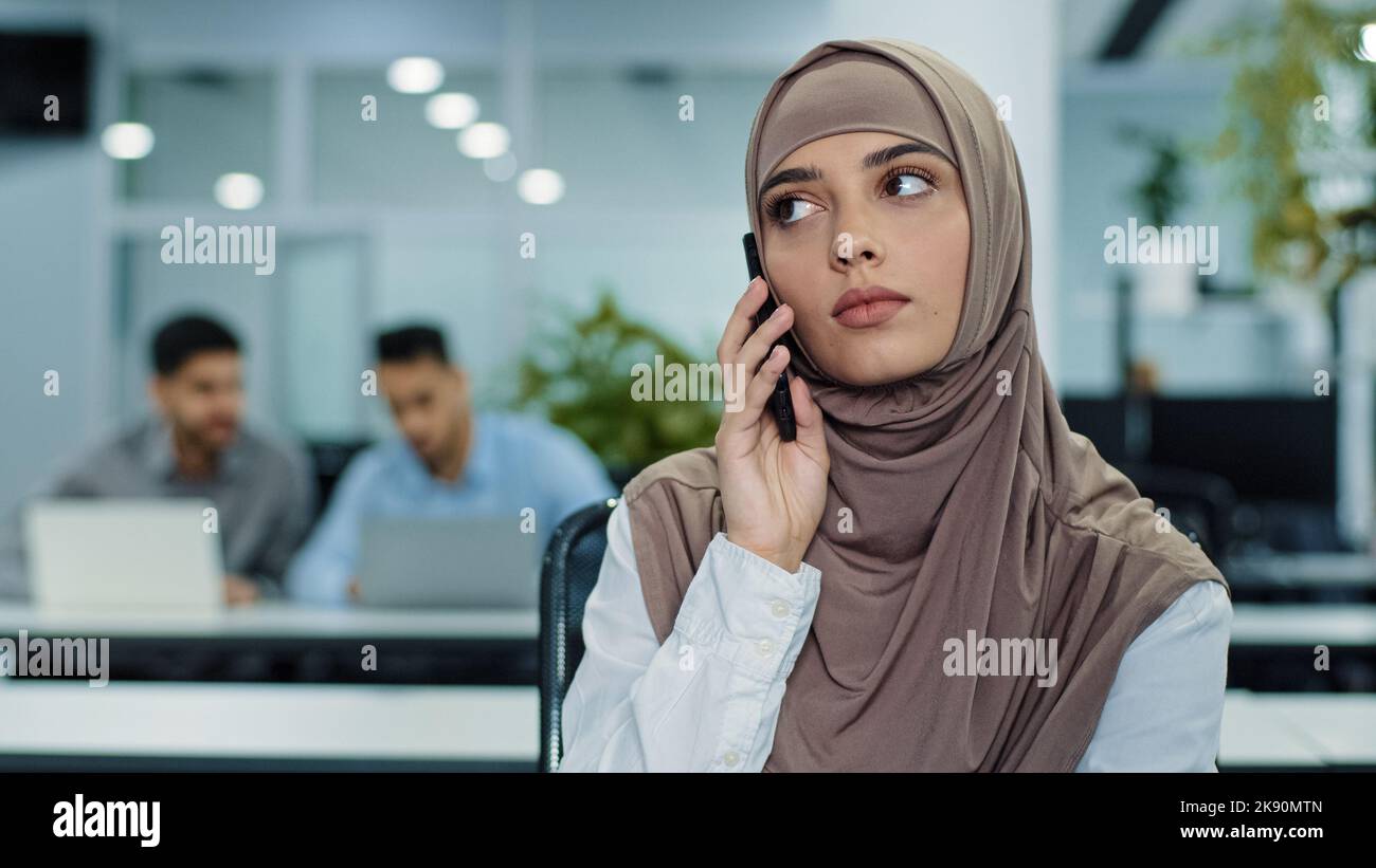 Responsable millénaire arabe sérieux et concentré dans le hijab parlant au téléphone, consultant, faisant un appel d'affaires au travail, jeune femme travailleur ou client Banque D'Images