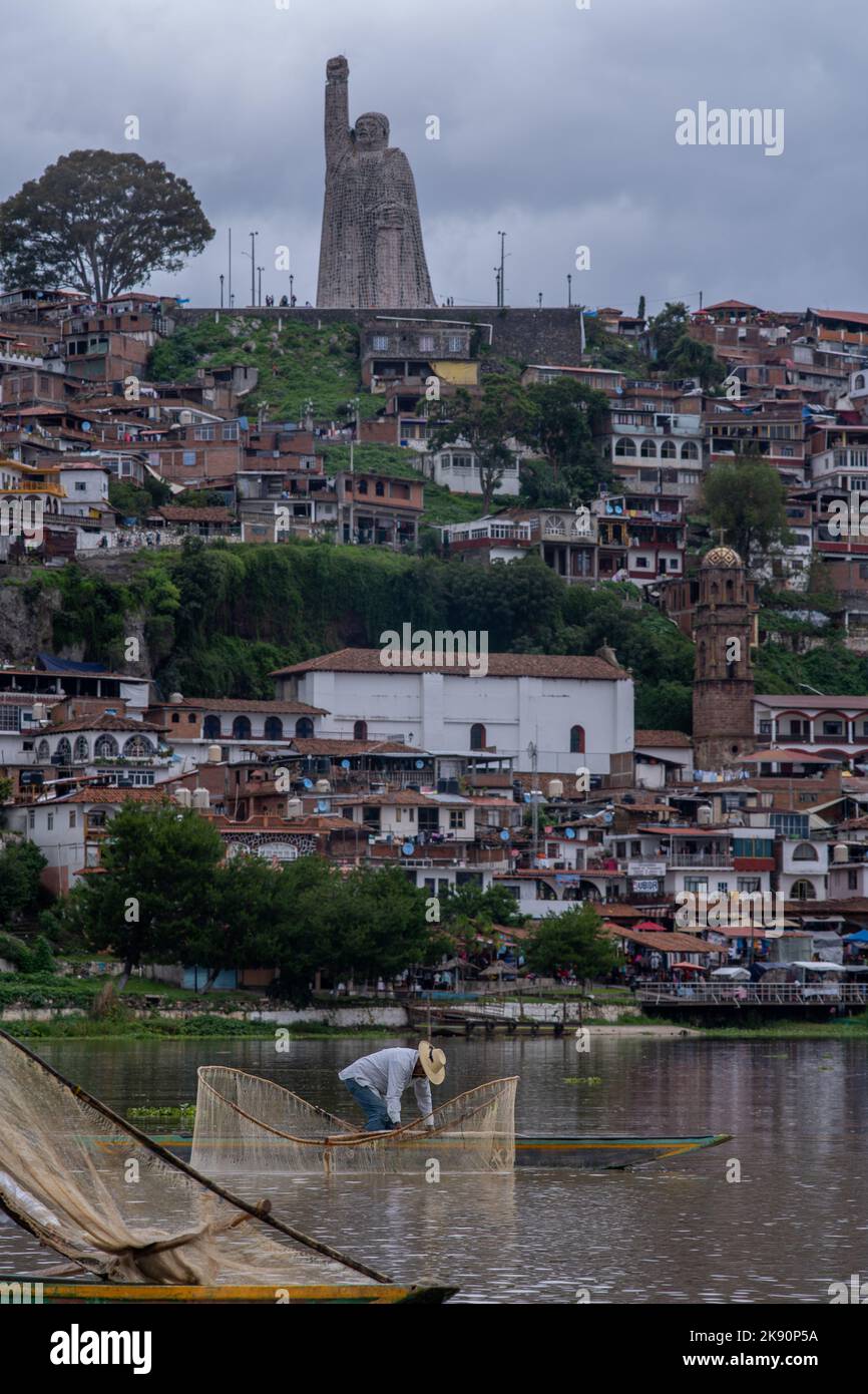 Une photo verticale d'un pêcheur sur un canoë avec la ville de Janitzio et une grande statue en arrière-plan Banque D'Images